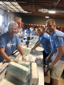 Three volunteers smile for the camera as they sort through diaper packets.