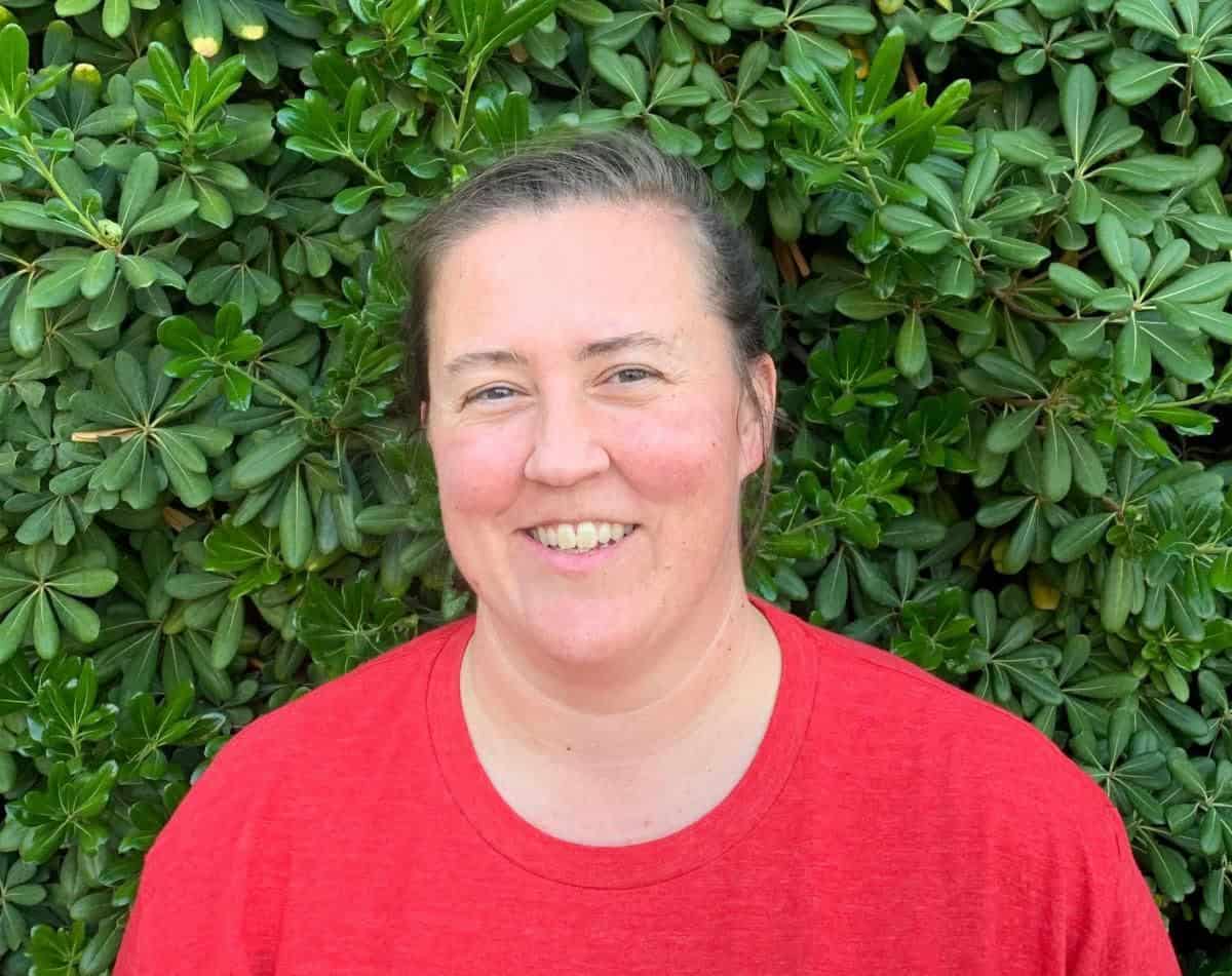 Volunteer management professional smiling outdoors in front of green foliage.