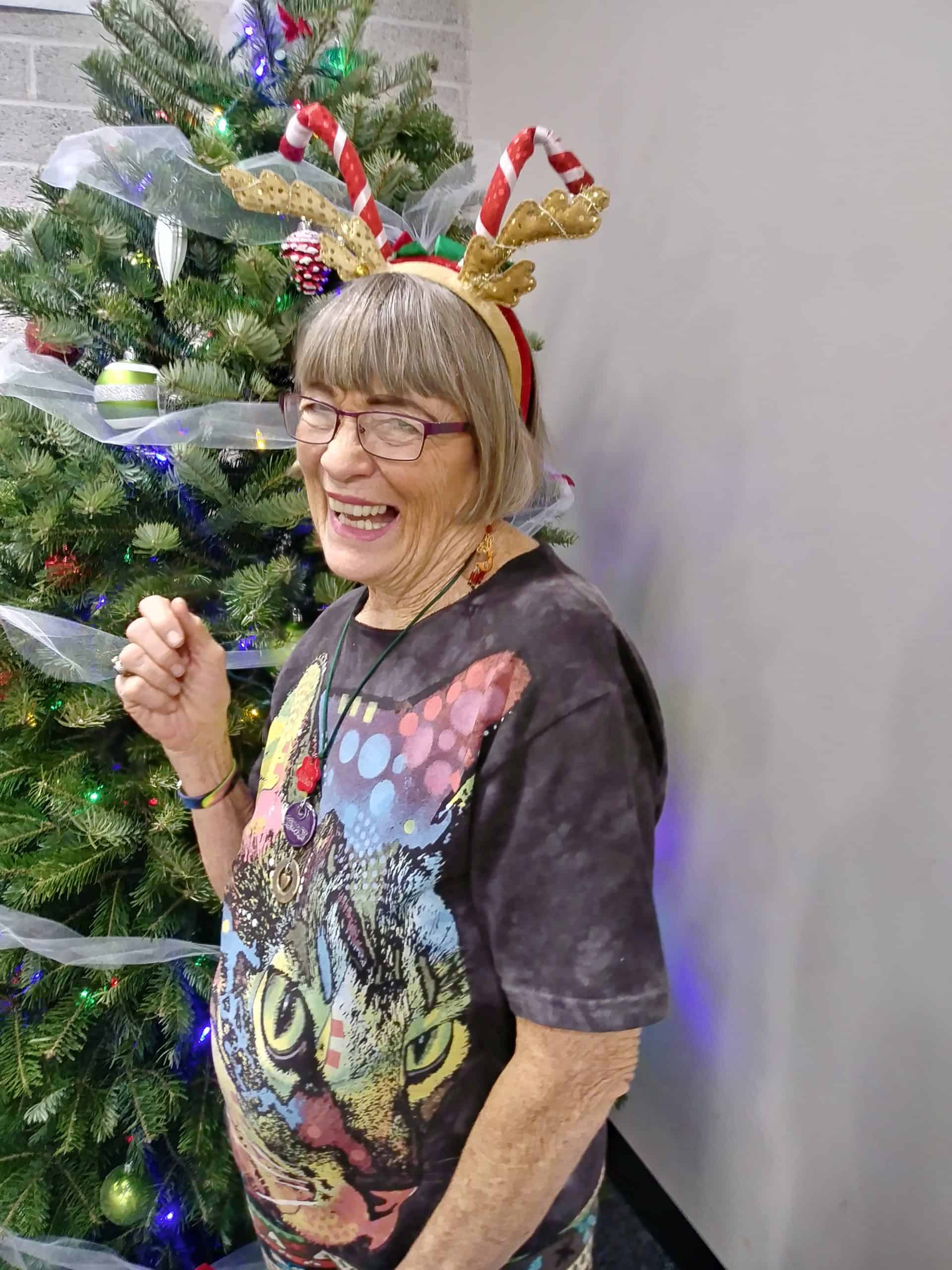 Festive woman wearing reindeer antlers headband near decorated Christmas tree.