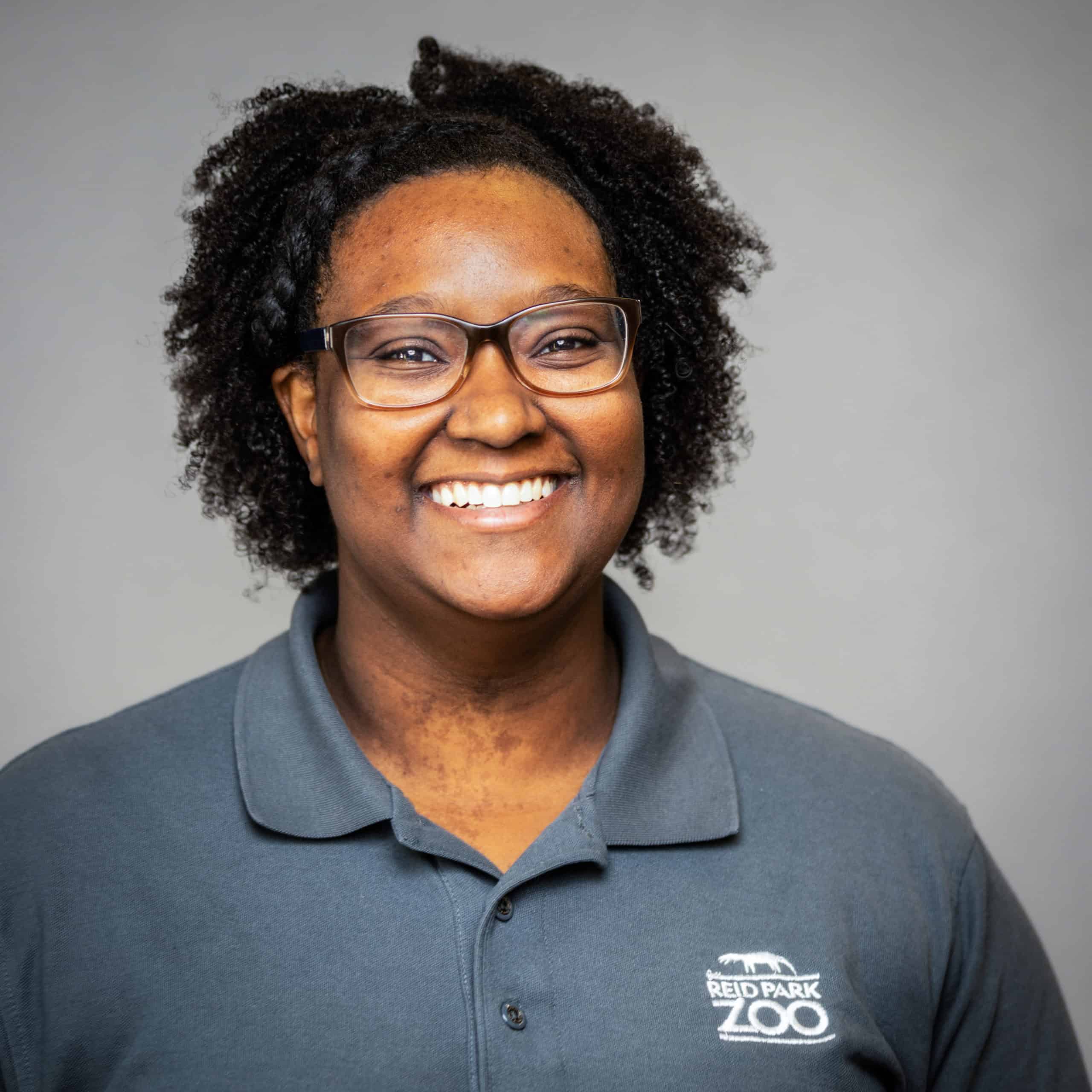 Volunteer management professional wearing a grey polo with Reed Park Zoo logo, smiling confidently.