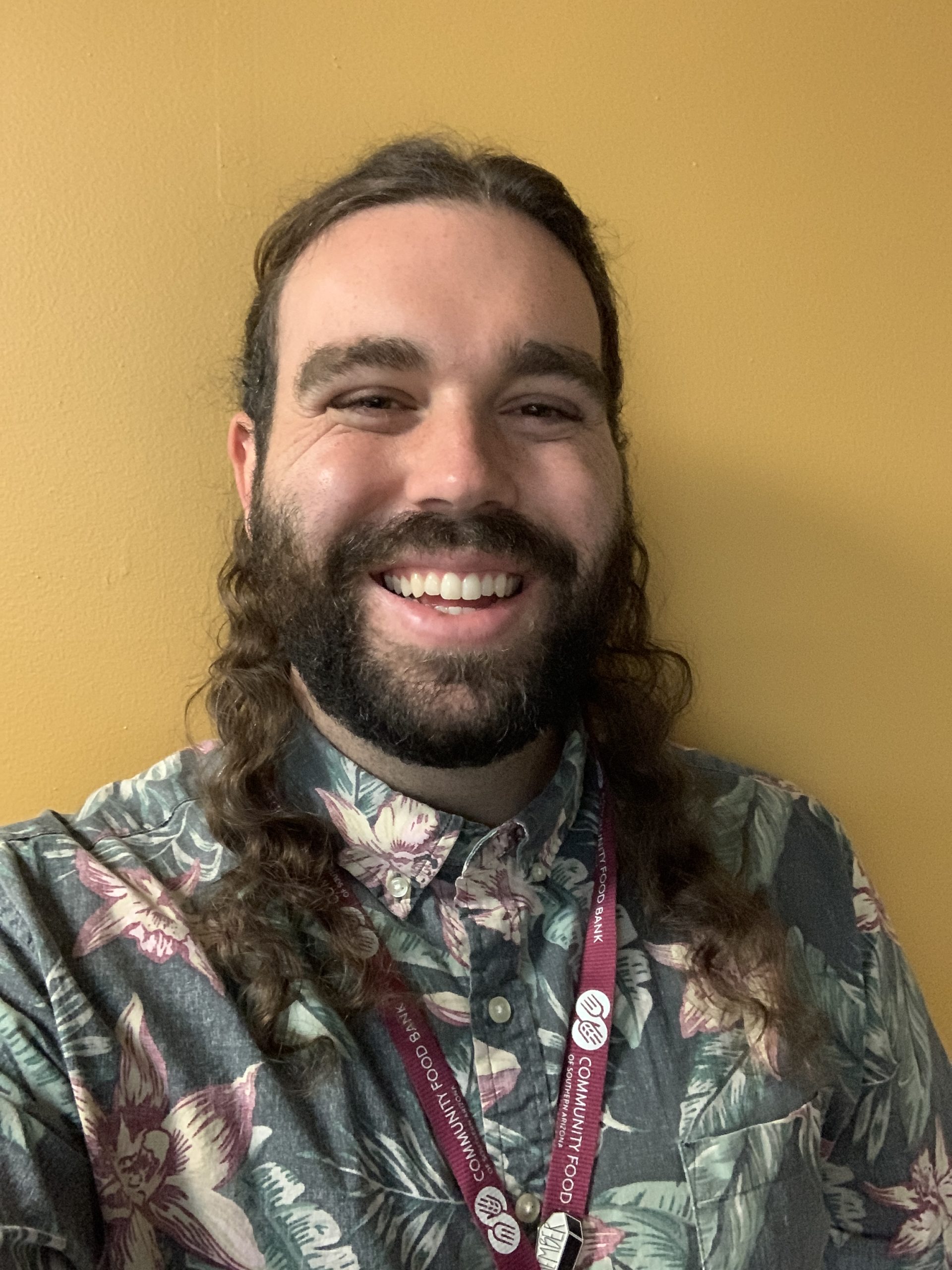 A man smiles at the camera in front of a yellow wall