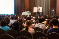 conference attendees watch speaker present in a large room