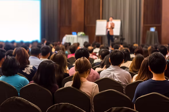 conference attendees watch speaker present in a large room