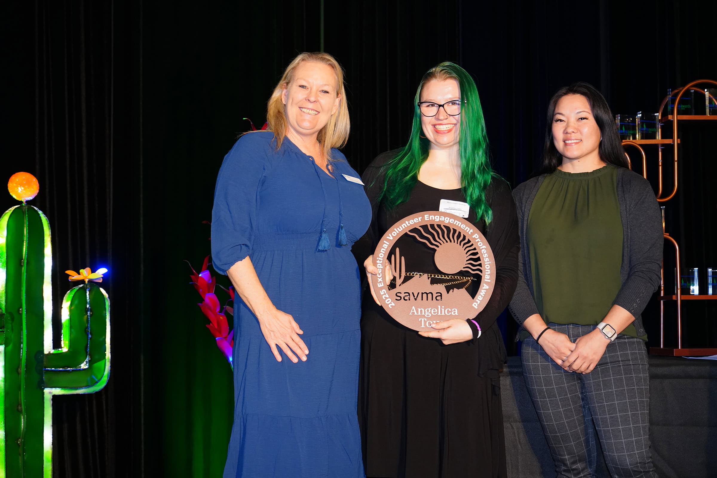 Three women at Volunteer Awards 2026 event, smiling on stage.